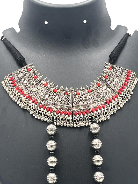 Ornate silver necklace with red stones on a black mannequin