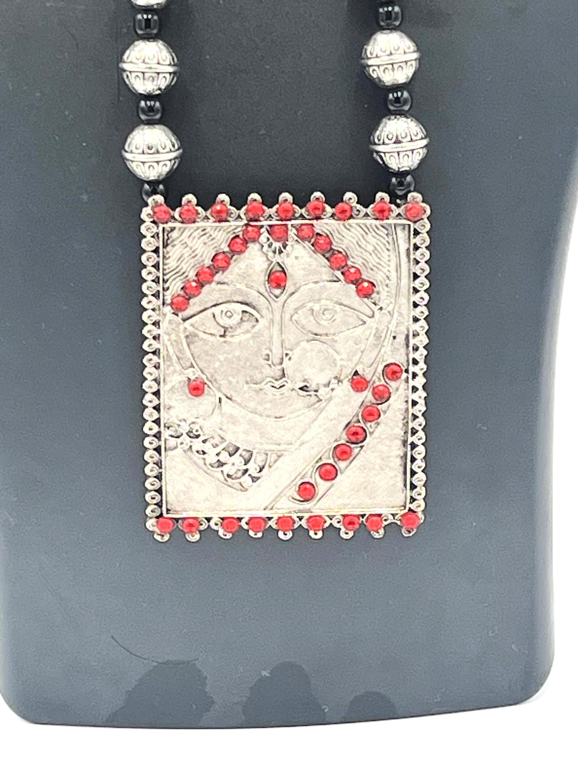 Necklace with a pendant featuring a face design and red stones on a gray background