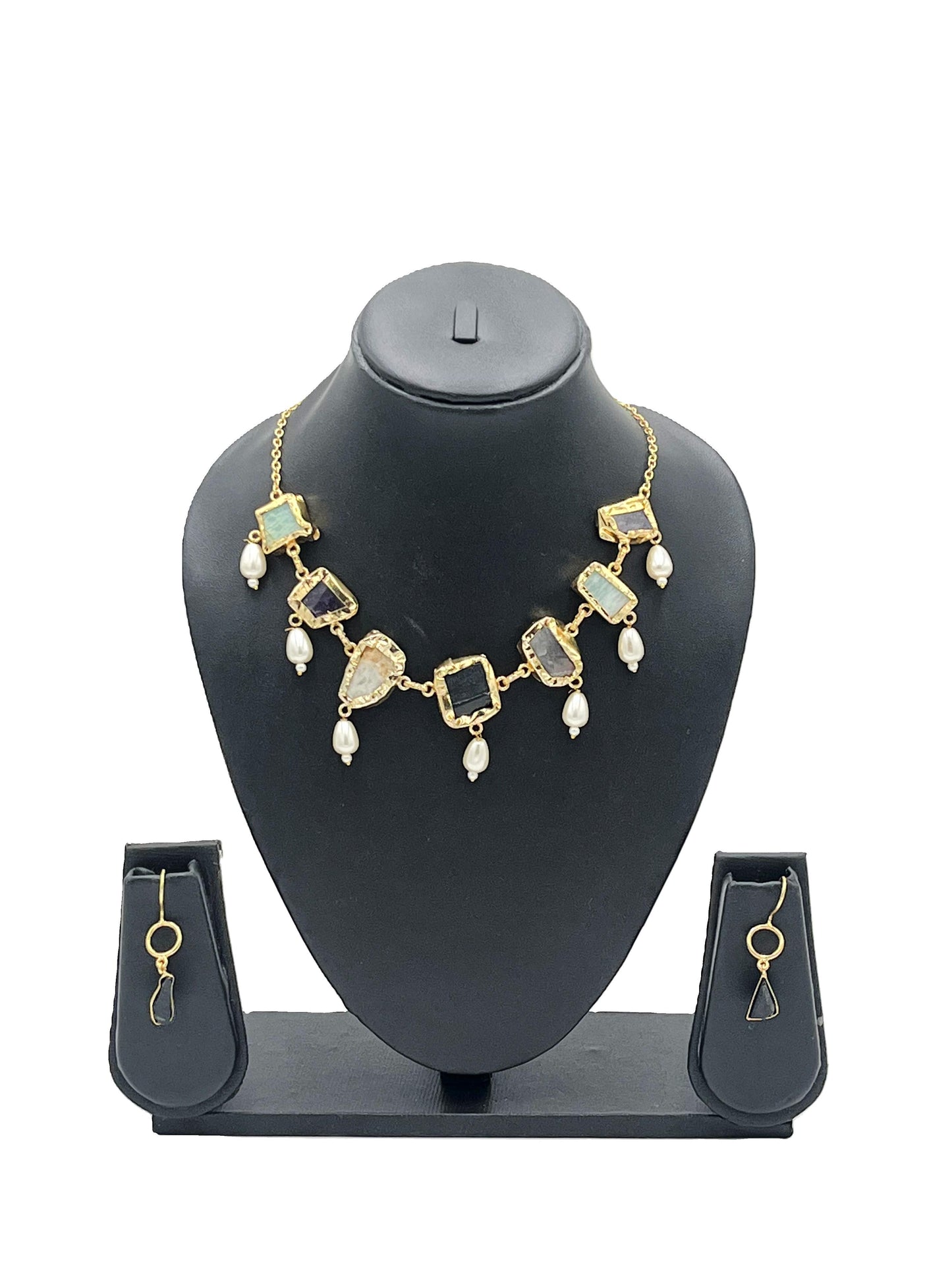 Gold necklace with green stones and pearl-like beads on a black mannequin bust, accompanied by matching earrings.