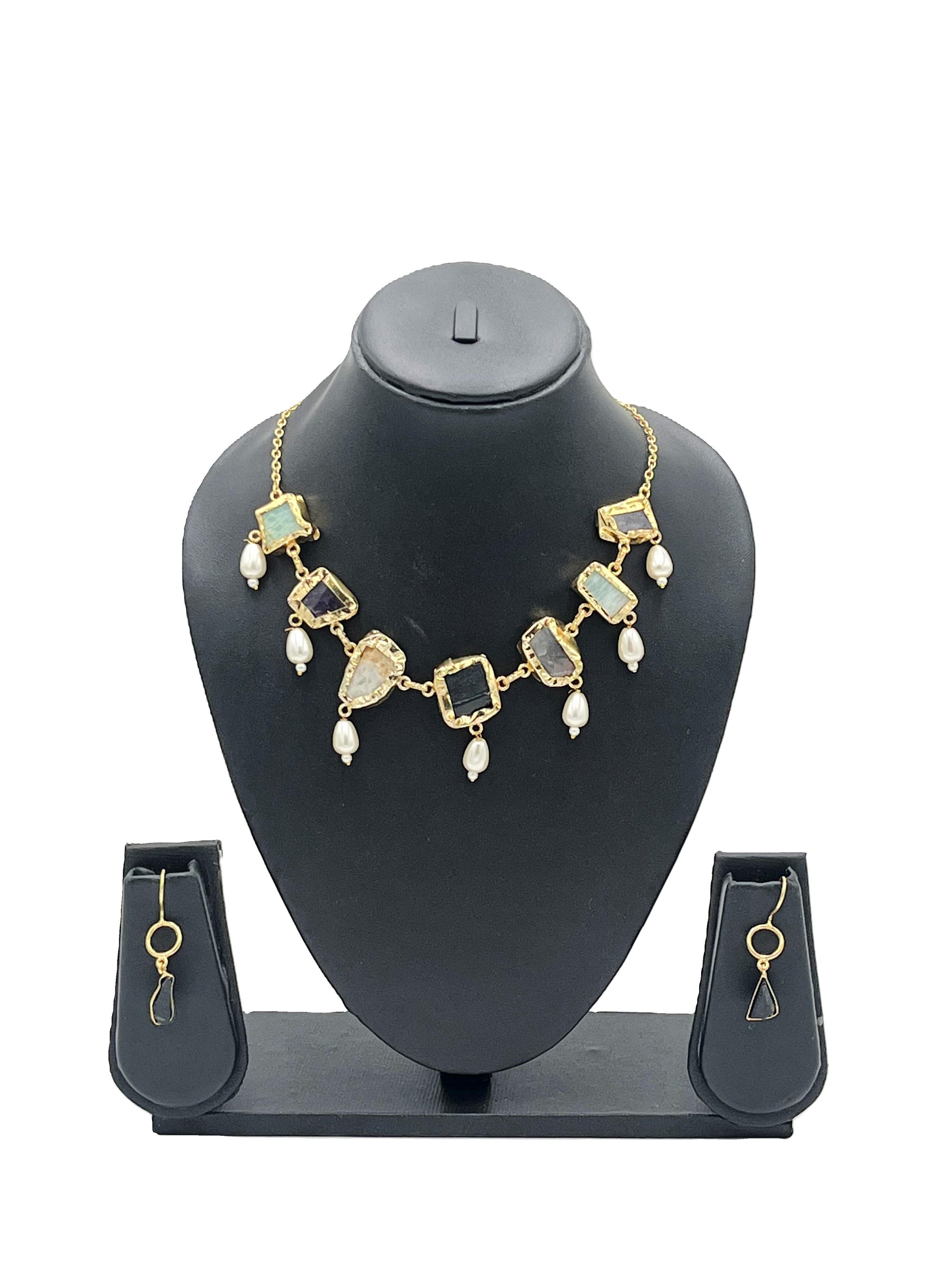Gold necklace with green stones and pearl-like beads on a black mannequin bust, accompanied by matching earrings.